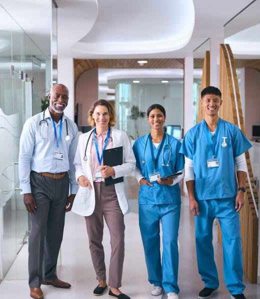 Portrait Of Smiling Multi Cultural Medical Team Wearing Scrubs And White Coats In Modern Hospital